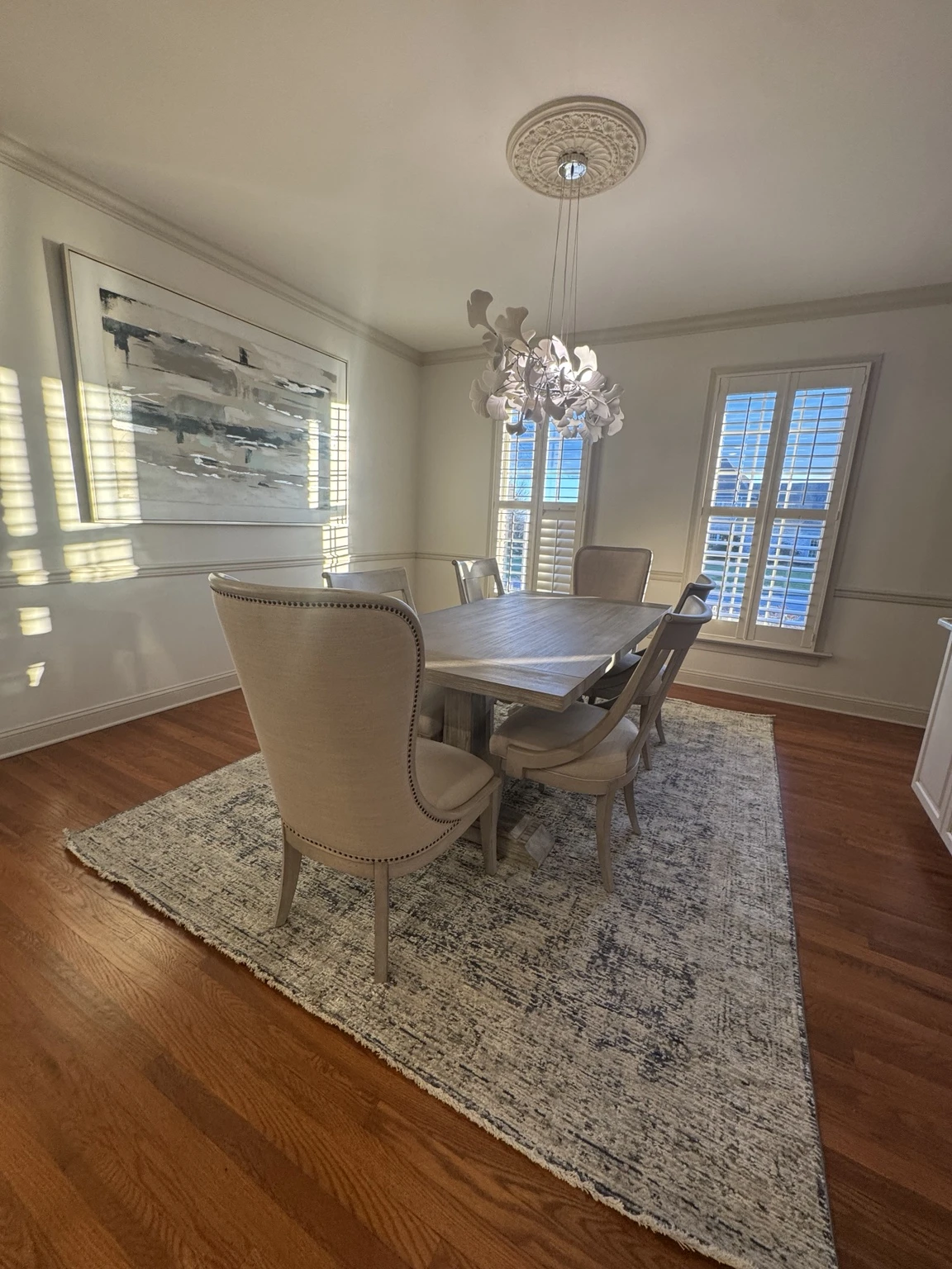 Dining room with a chandelier, upholstered chairs and white window shutters